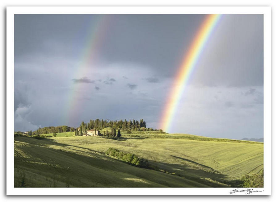 Paesaggio collinare toscano, con doppio arcobaleno e casolare in lontananza.